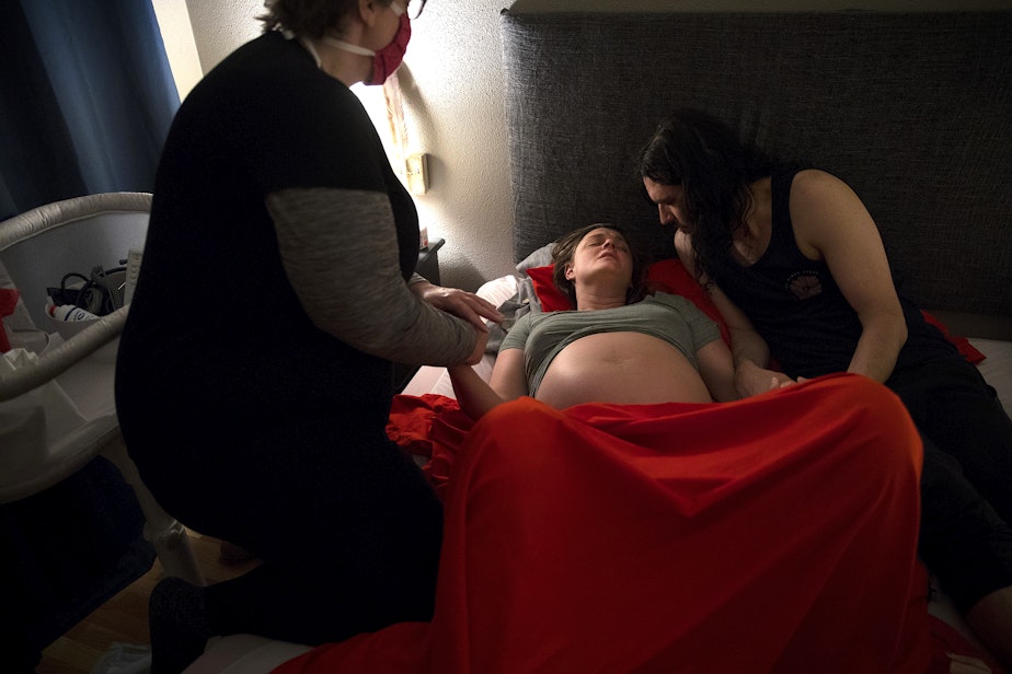 caption: Midwife Jenn Linstad, left, and Jake Black, right, hold Hope Black's hands as she breathes through a contraction at 2:25 a.m. on Friday, May 29, 2020, at the couple's home on Vashon Island. Hope and Jack Black opted for a home birth, changing their birth plan, as a result of the coronavirus.